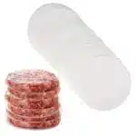 Stack of raw burger patties separated by clear cellophane patty discs, next to a roll of patty discs